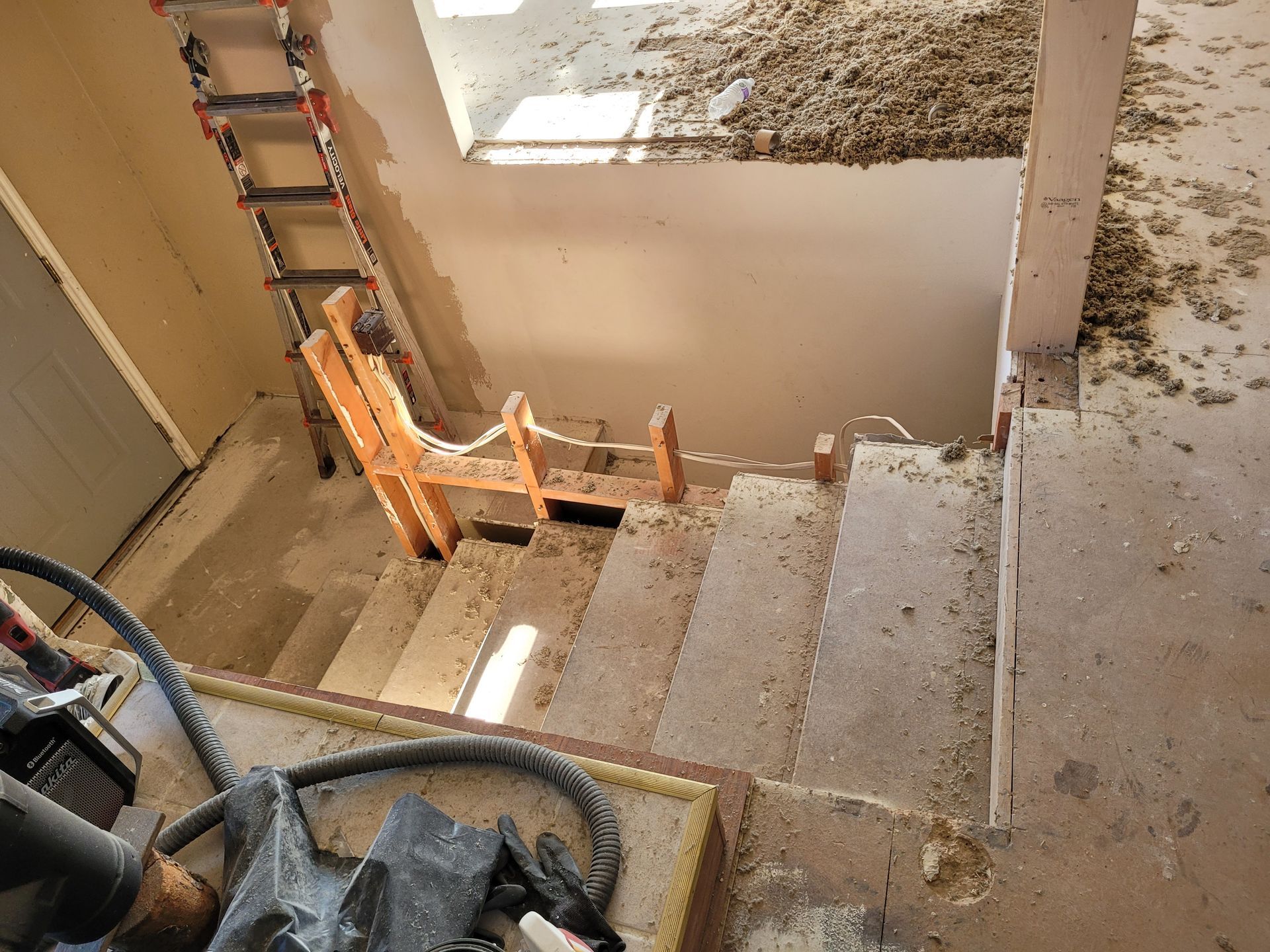 Concrete staircase under construction, with a wooden safety barrier blocking the lower steps. A ladder and construction debris are present.