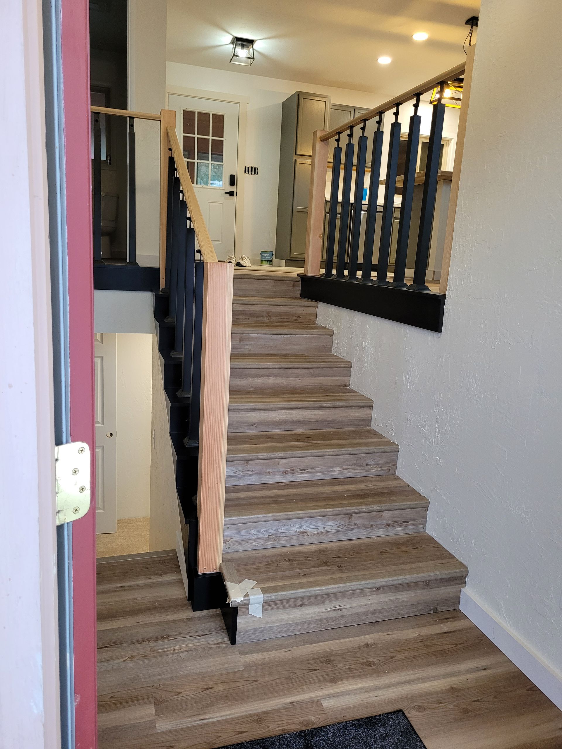 Staircase with black banisters and a light-colored wooden handrail leading down to a white door, likely in a home.