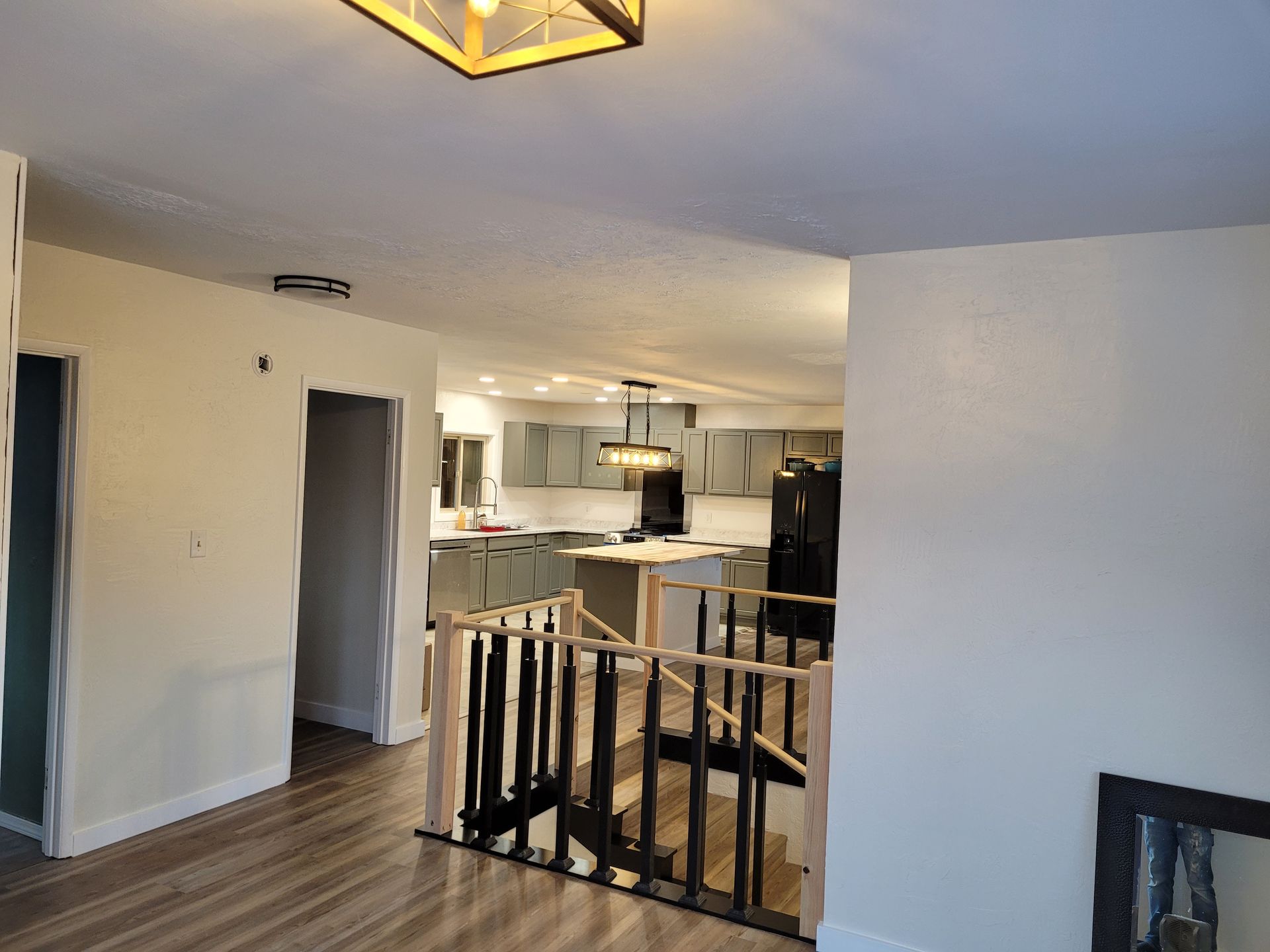 Interior view of a home with a staircase leading to a kitchen. Light walls, wood floors, and a black and gold railing.
