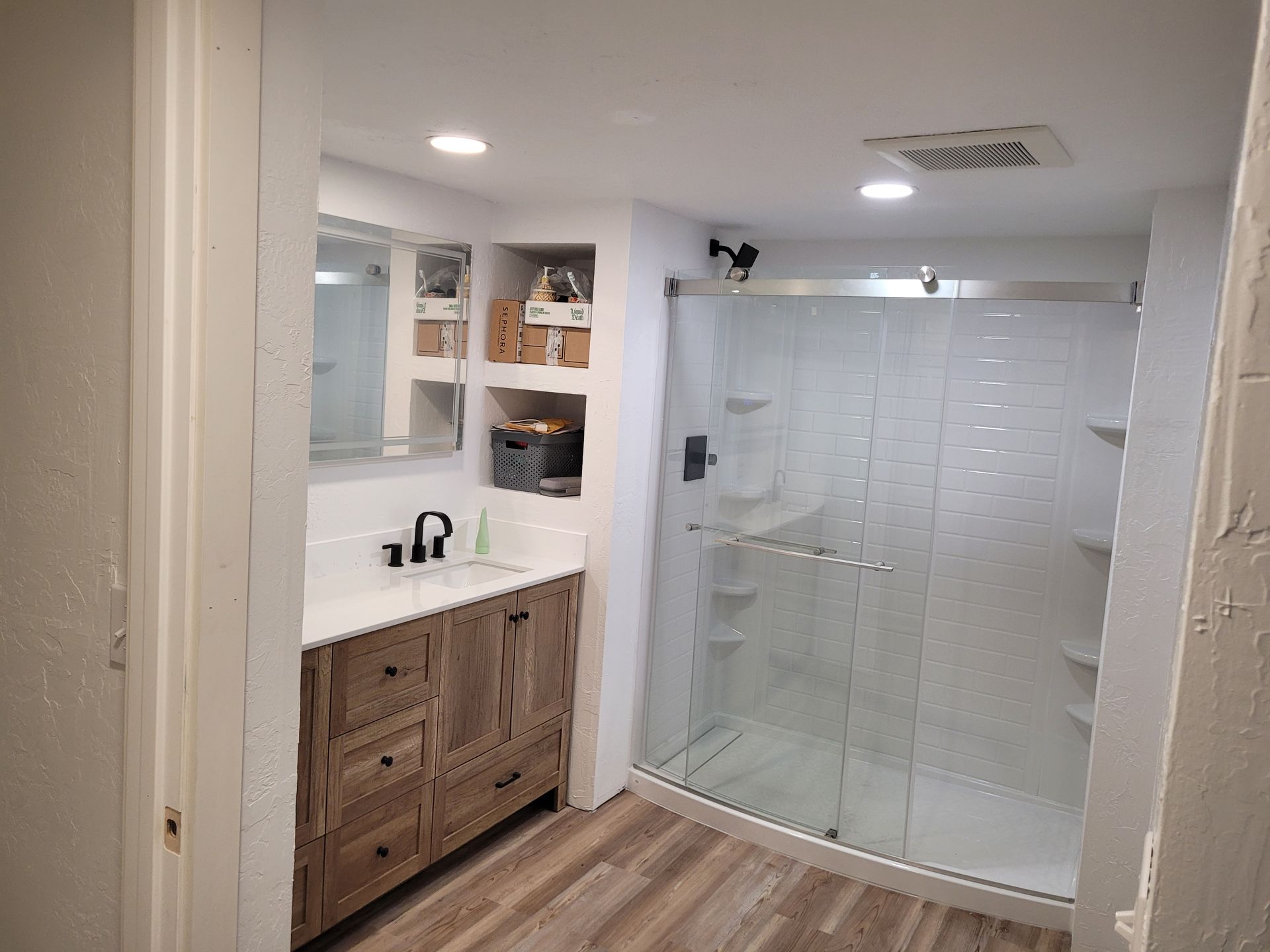 Interior view of a home showing the entryway and kitchen. Light-colored walls and floors with dark railings. The kitchen has gray cabinets.