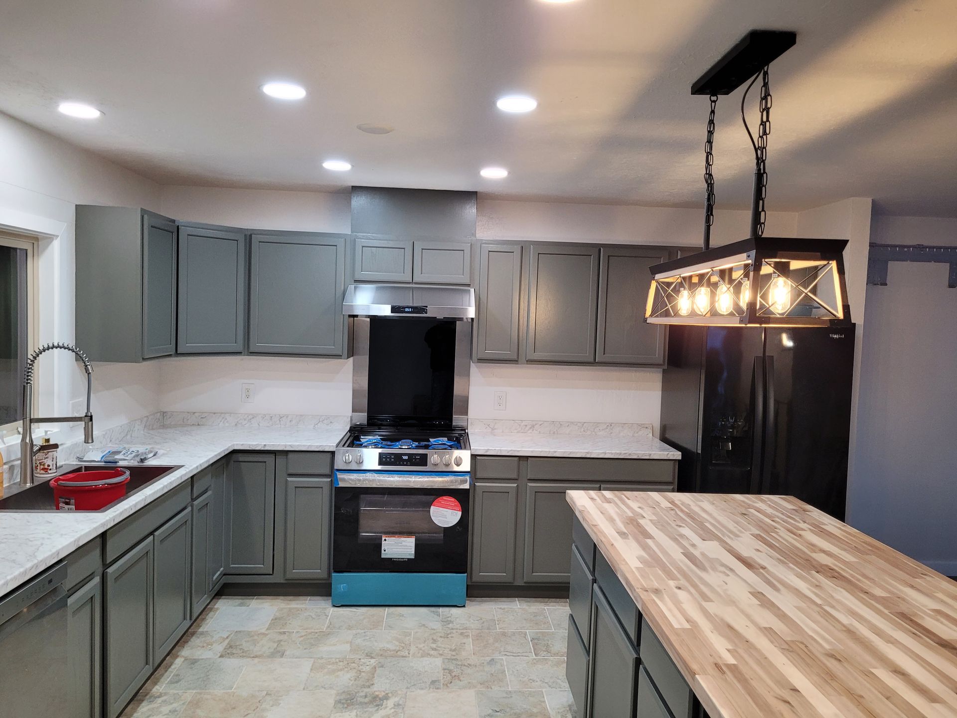 Gray kitchen with cabinets, stainless steel appliances, and a butcher block island. A black light fixture hangs over the island.