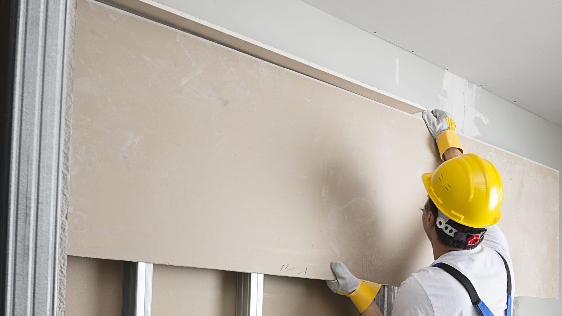 A man is installing drywall on a wall.