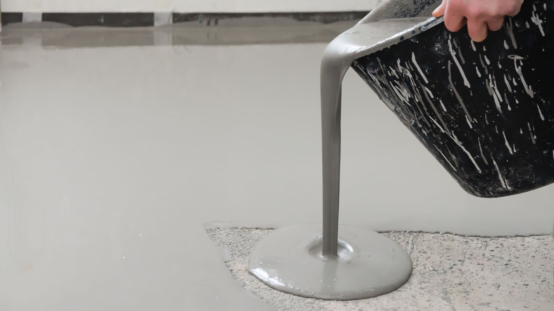 A person is pouring concrete into a hole in the floor.