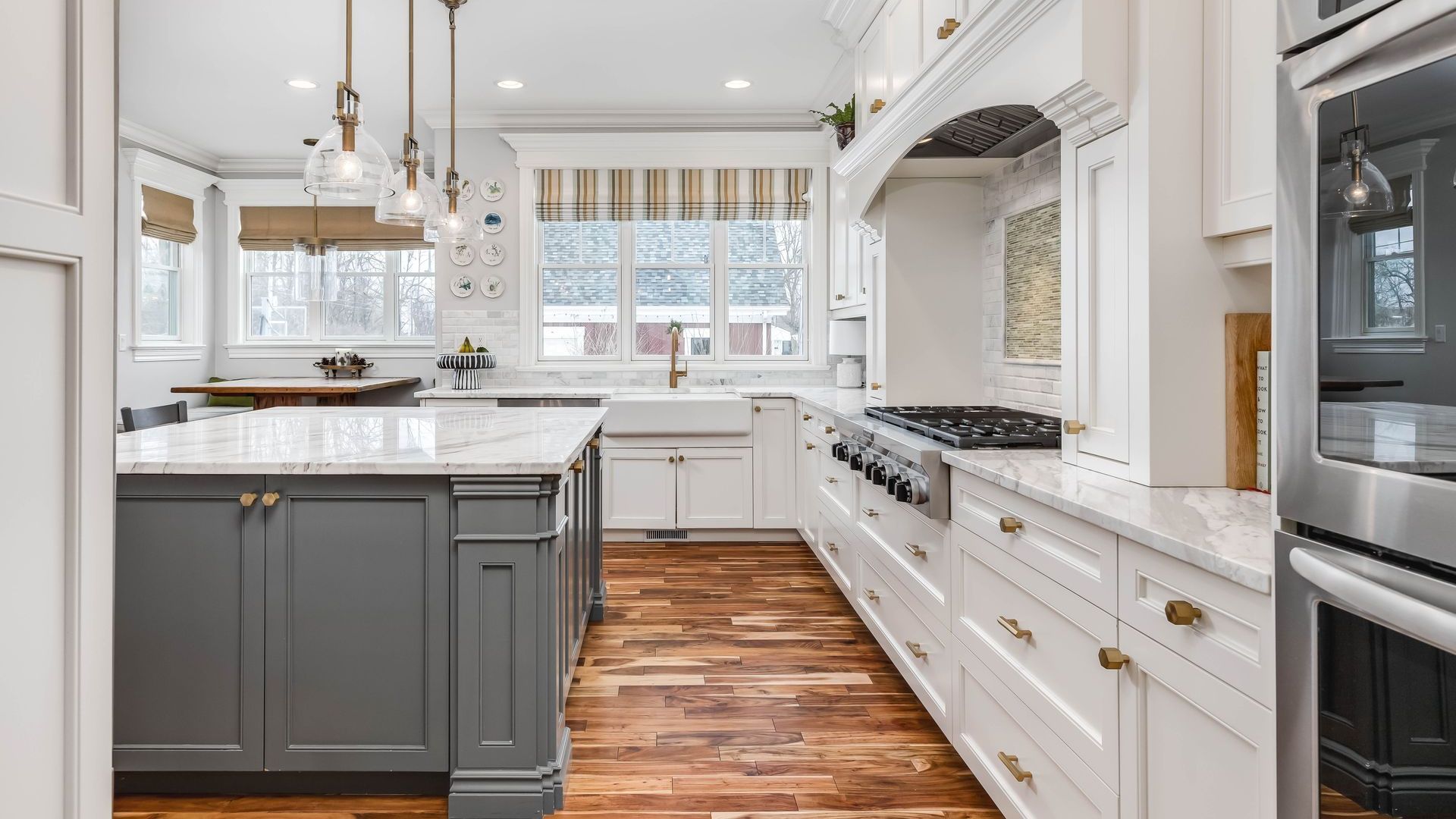 A kitchen with white cabinets , stainless steel appliances , wooden floors and a large island.