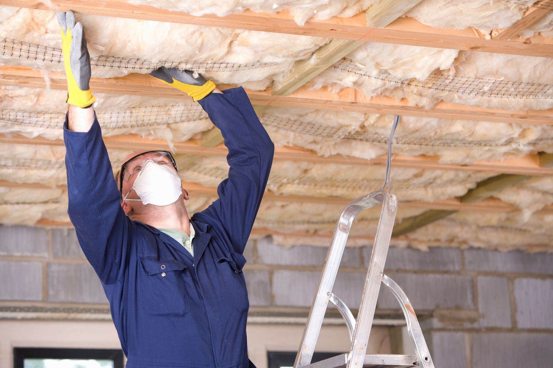 A man wearing a mask and gloves is working on a ceiling.