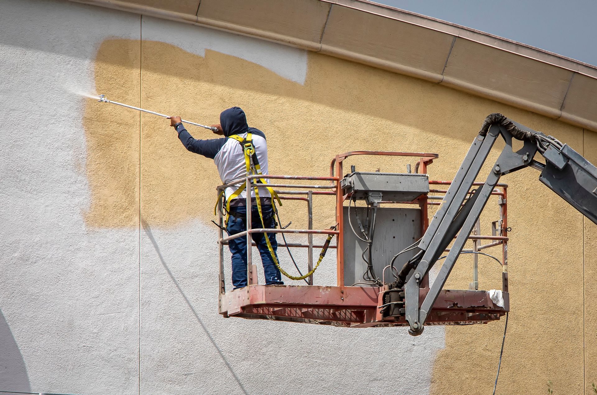 A man is painting the side of a building on a crane.