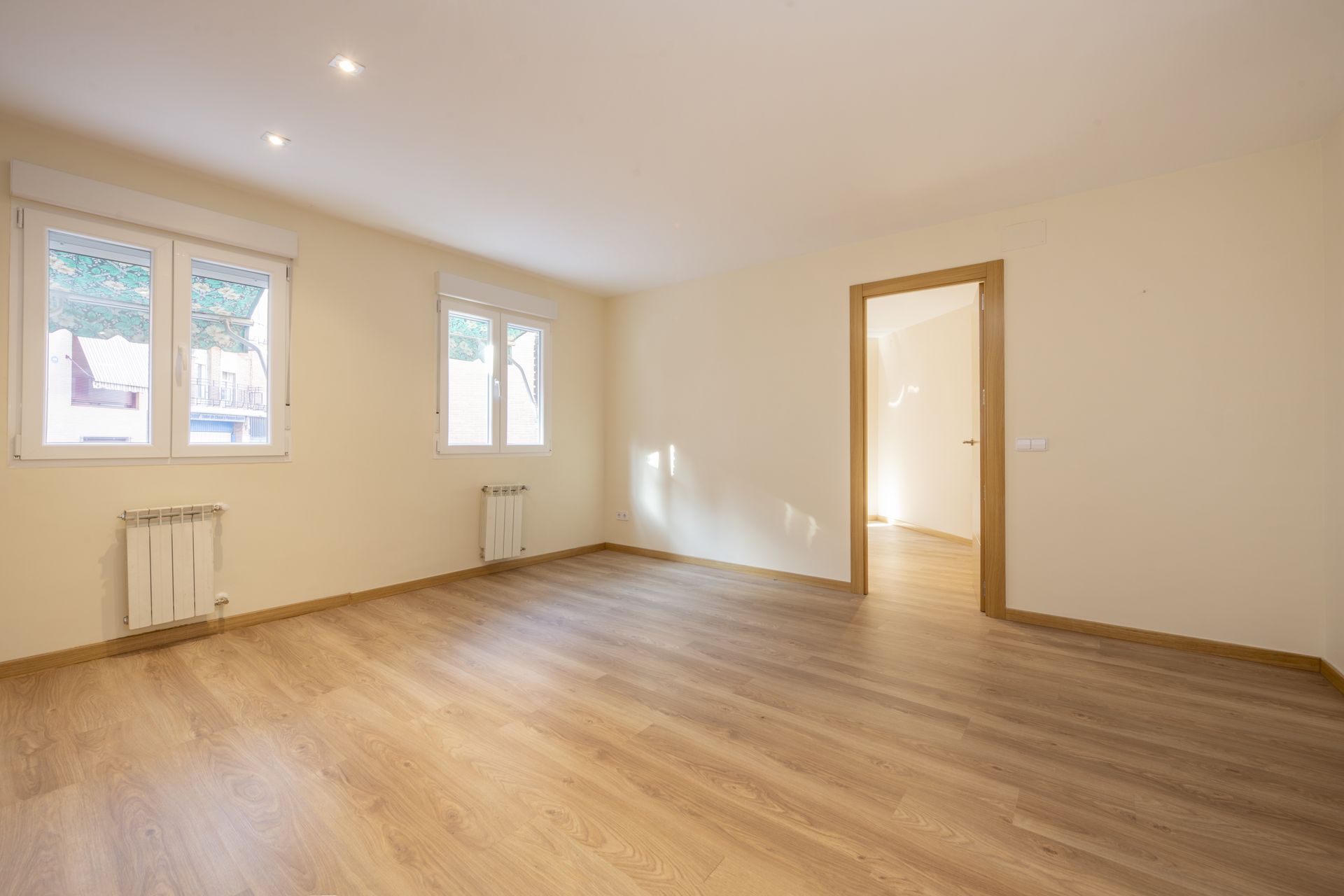 An empty living room with hardwood floors and two windows.
