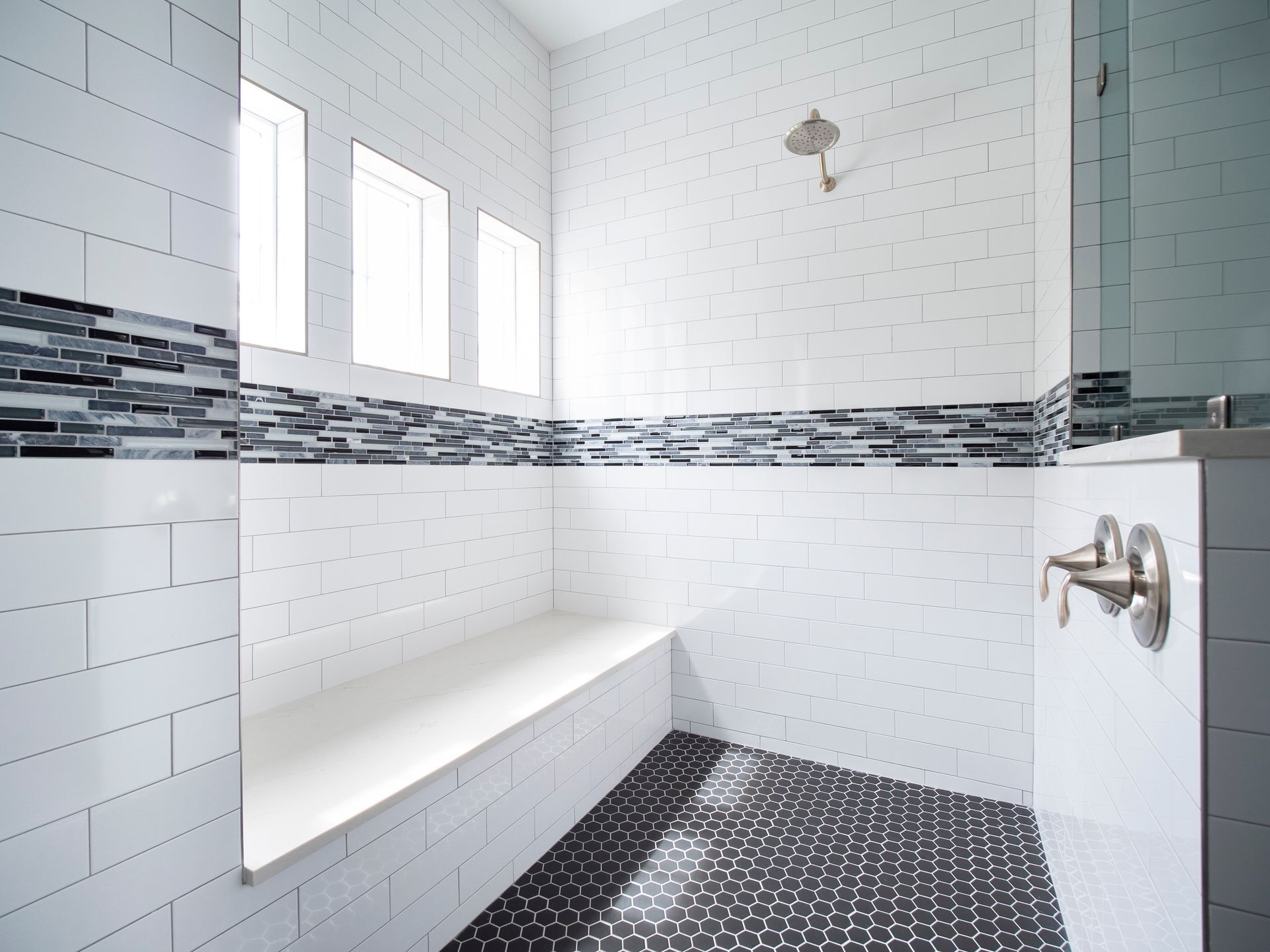 A bathroom with white tiles and black tiles and a shower with a bench.