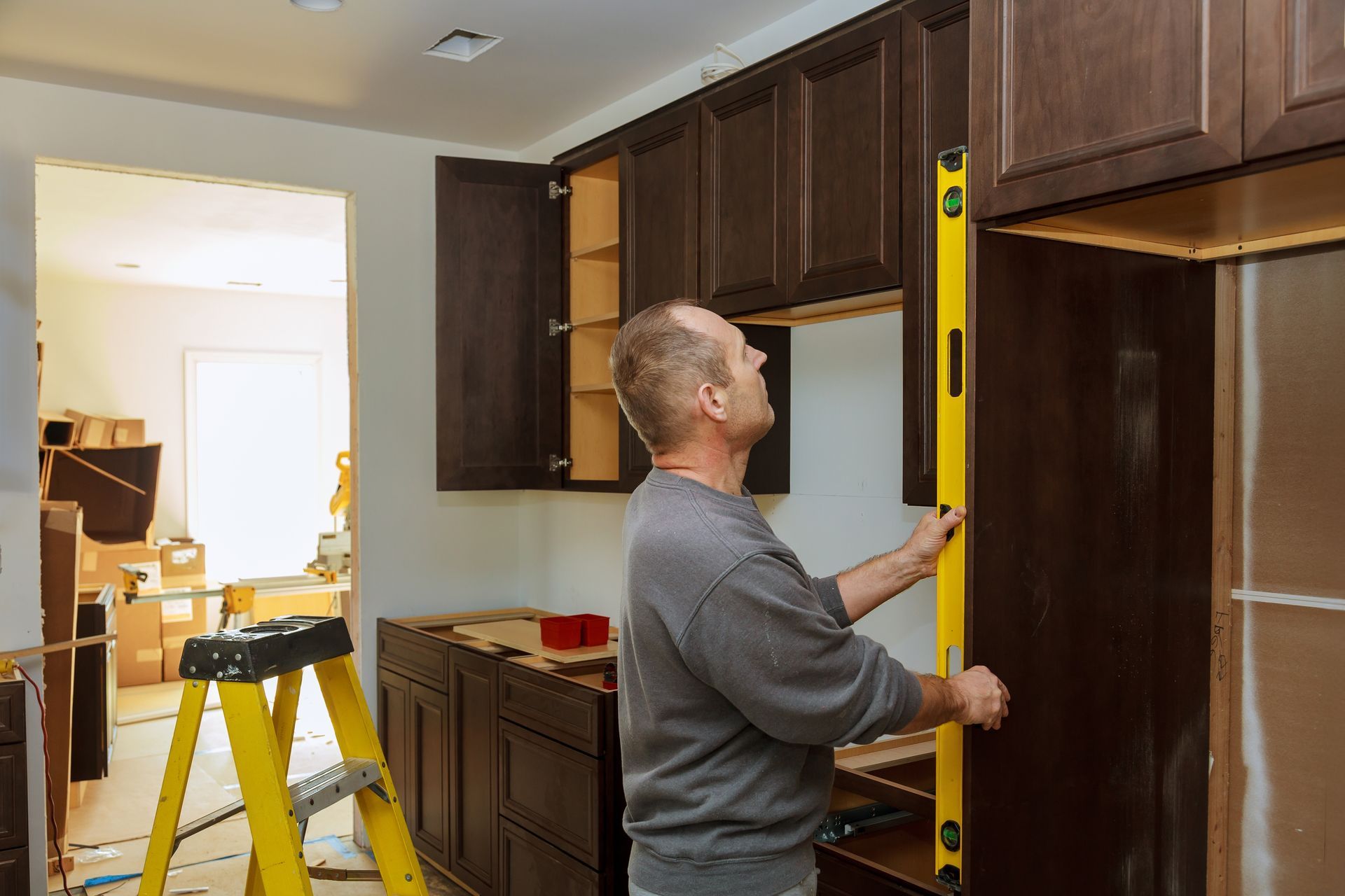 A man is measuring a cabinet with a level in a kitchen.