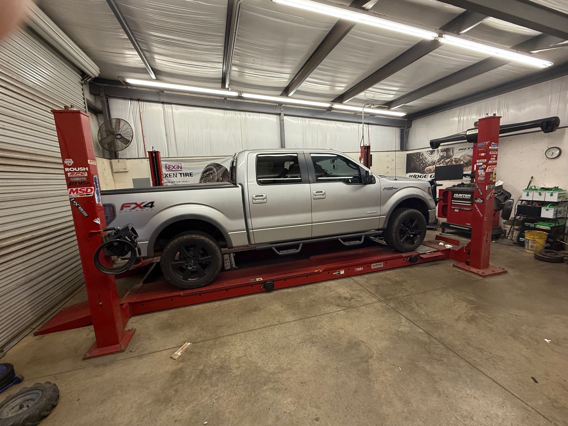 Silver pickup truck on a red car lift inside a workshop.