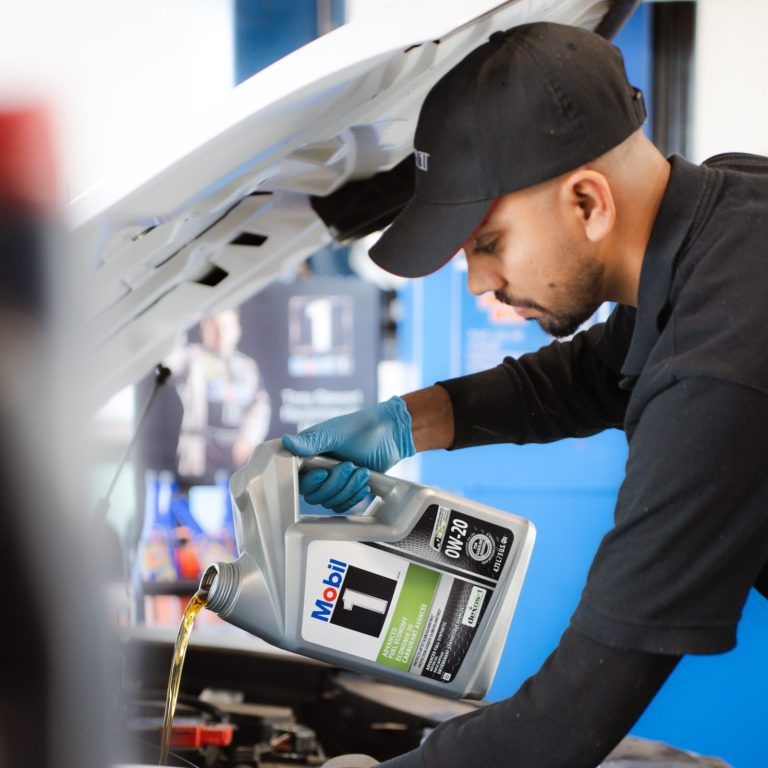 Mechanic pouring motor oil into a car engine in a garage.