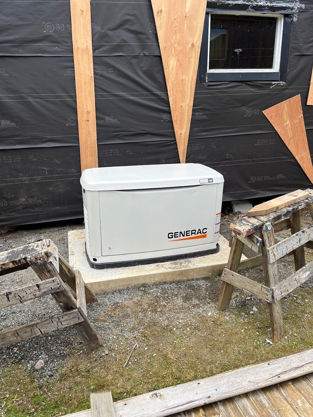 A Generac generator sits on a concrete pad outside a building under construction.