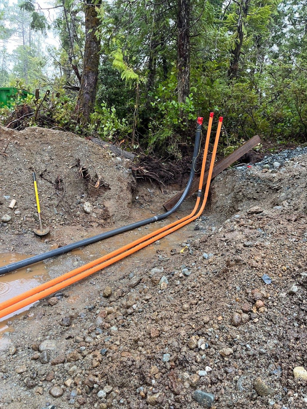 Orange and black conduits in a muddy trench with trees in the background.