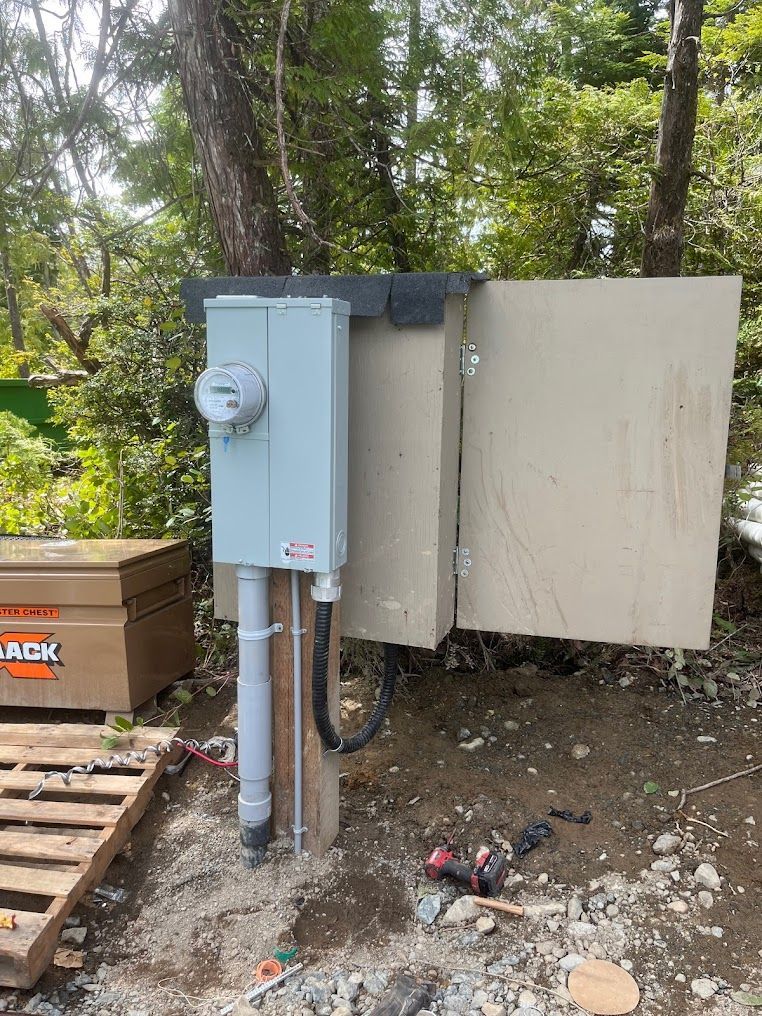 Electrical meter box on a wooden post outdoors, light blue with beige enclosure. Tools and wood debris surround.