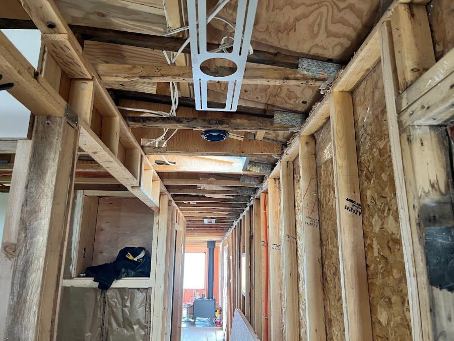 Interior hallway under construction; exposed wooden studs, ceiling beams, and wiring.