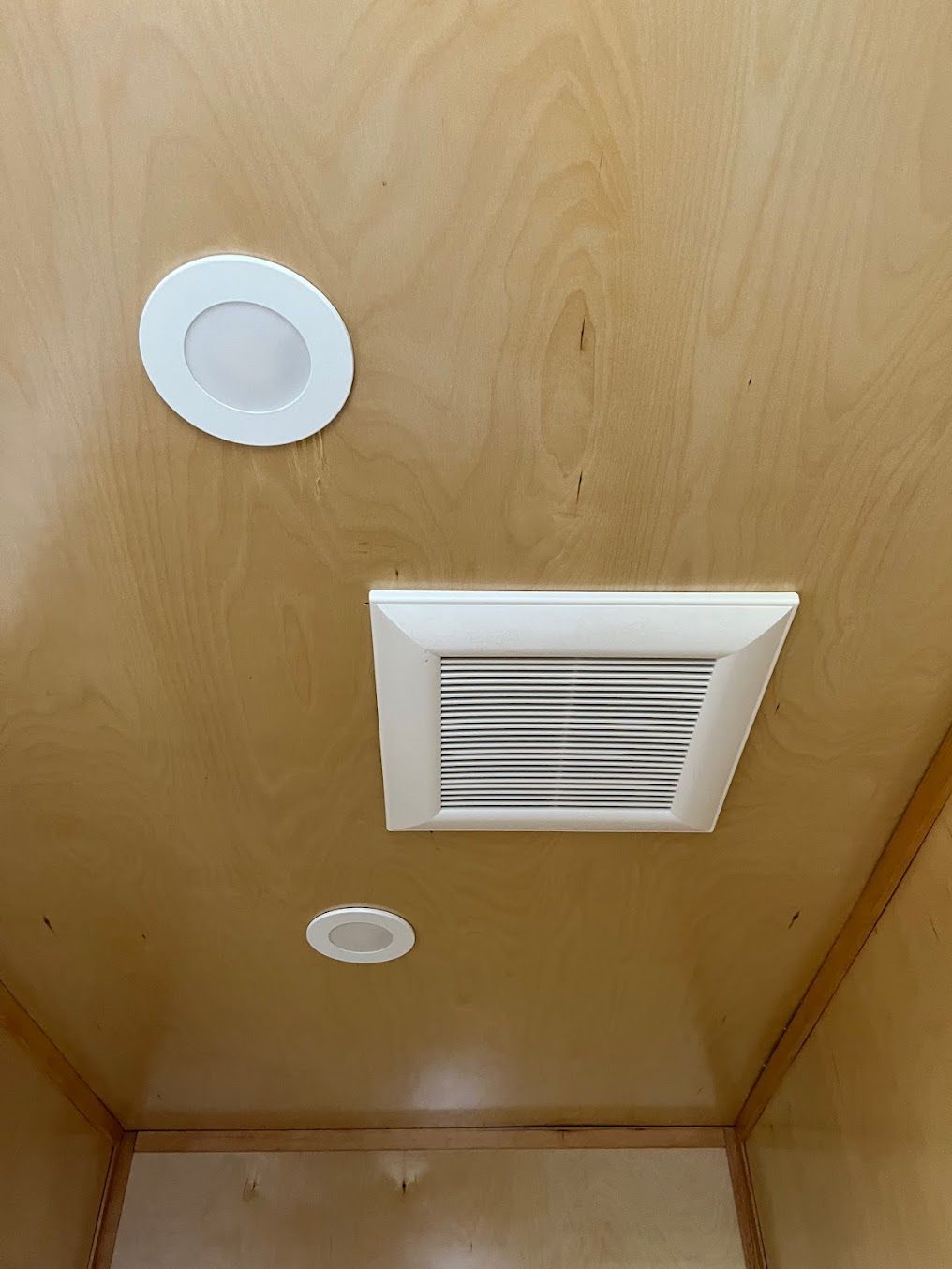 Ceiling with two recessed lights and a square air vent. Wood paneling.