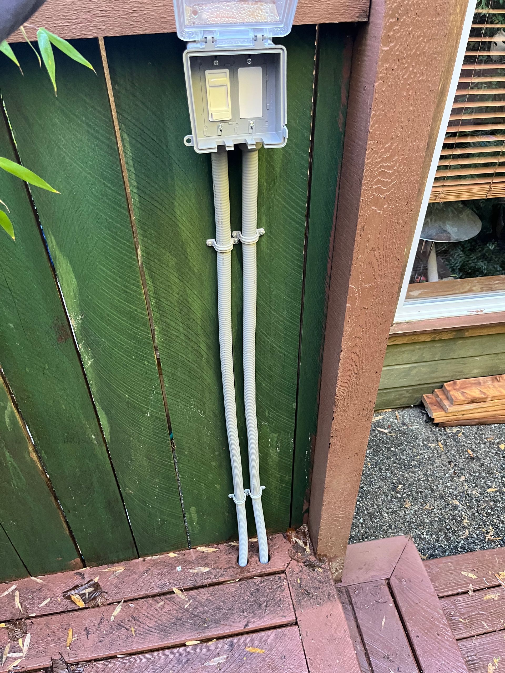Trench dug in the ground with gray pipes and caution tape. Dirt piles nearby; grass and debris around.