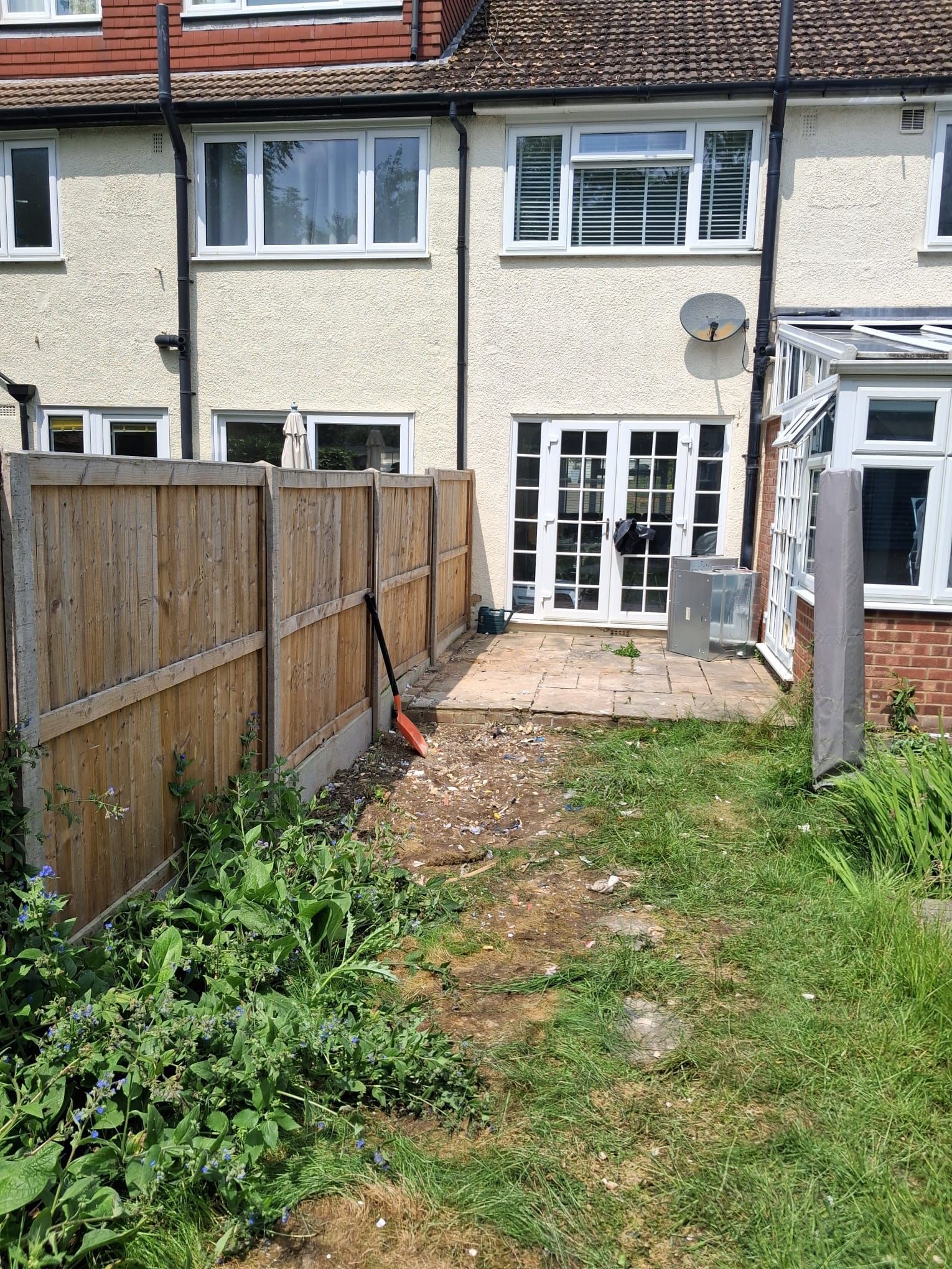 Backyard with a wooden fence, patio, overgrown grass, and a view of a house's French doors.