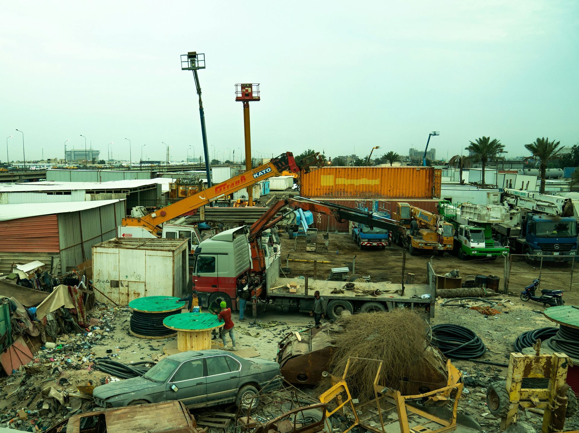 Construction site with cranes, trucks, and debris under an overcast sky.