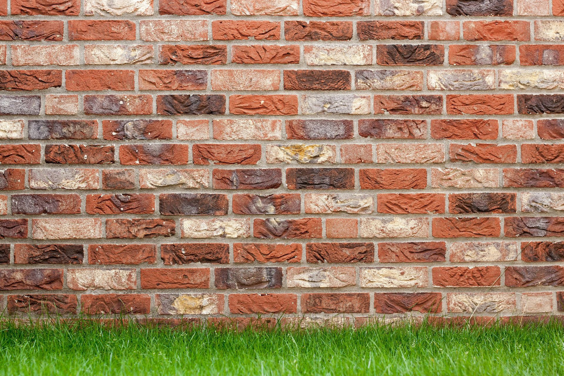 Brick wall with varying shades of red and brown bricks above a strip of bright green grass.