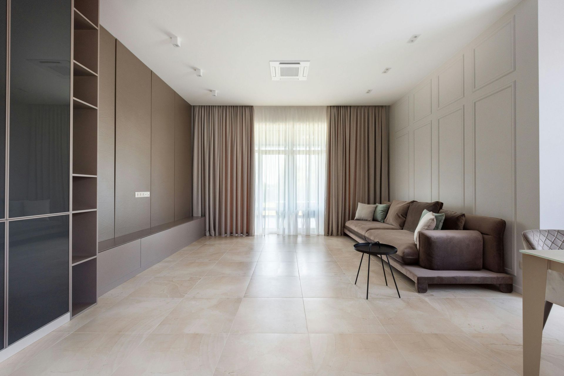 Modern living room with a brown sofa, beige walls, and light-colored flooring.