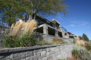 A large house is sitting on top of a hill next to a stone wall.