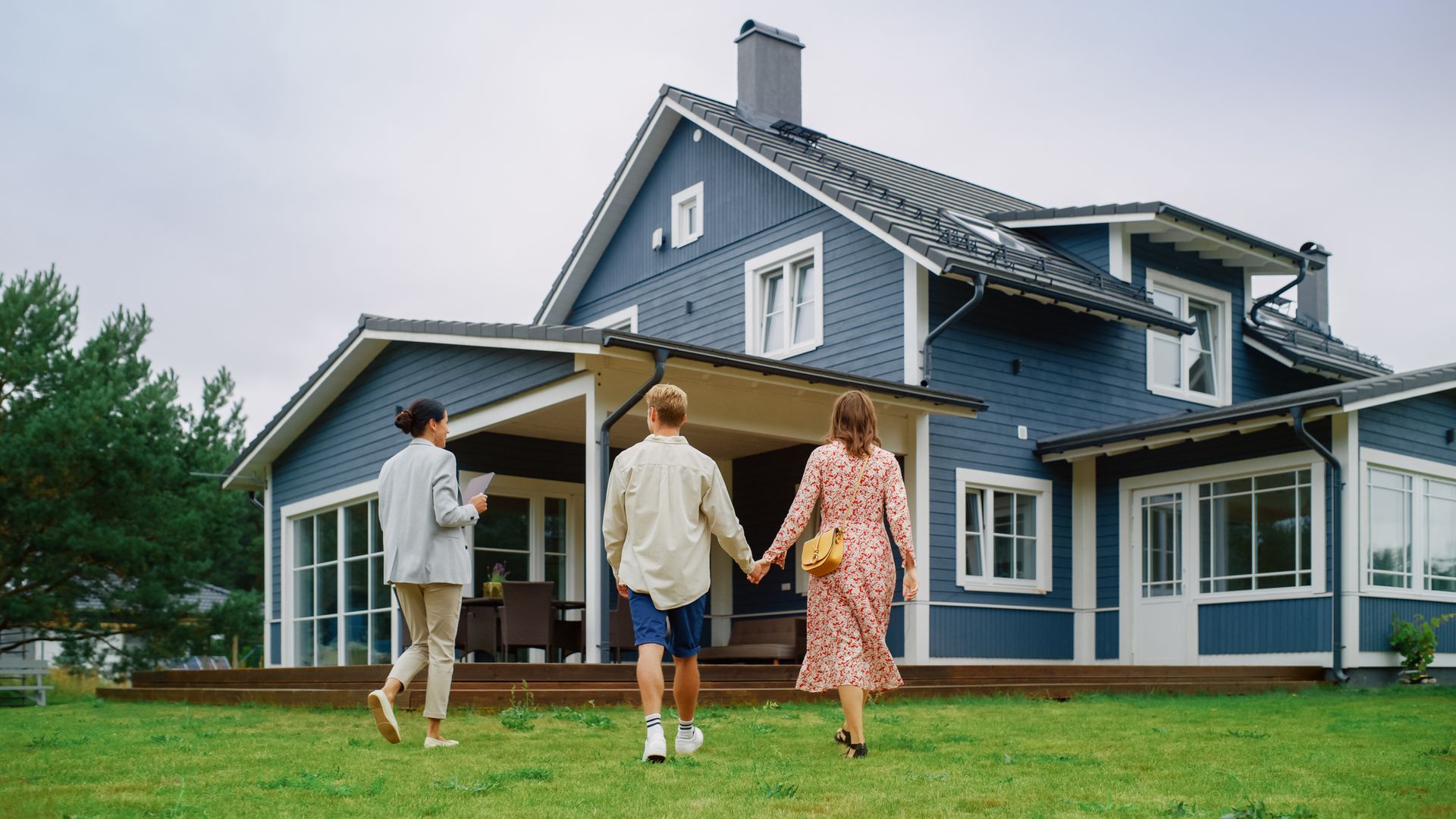 A family is walking towards a blue house holding hands.