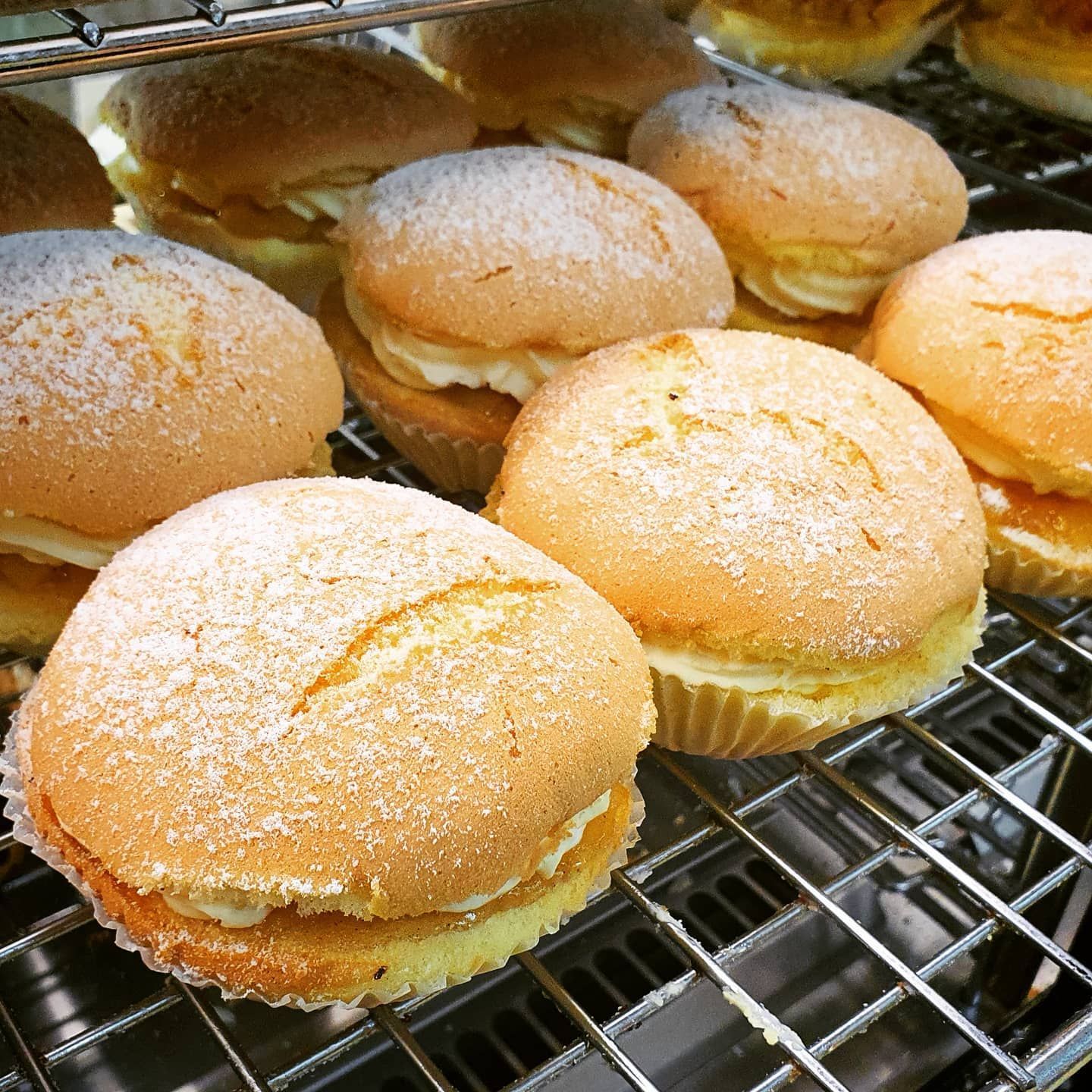 Close-up of sponge cakes with cream filling, dusted with powdered sugar, displayed on a wire rack.
