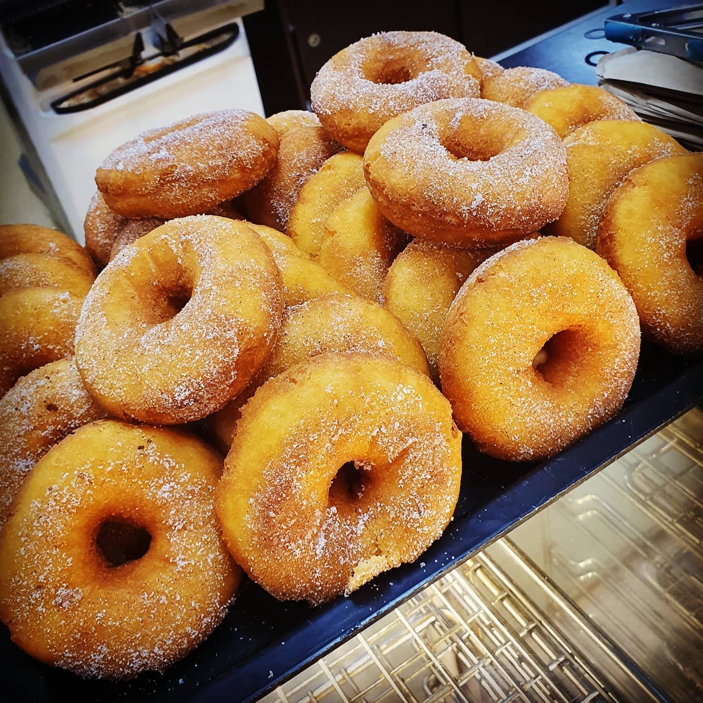Pile of golden, sugar-coated donuts on a blue tray, ready to eat.