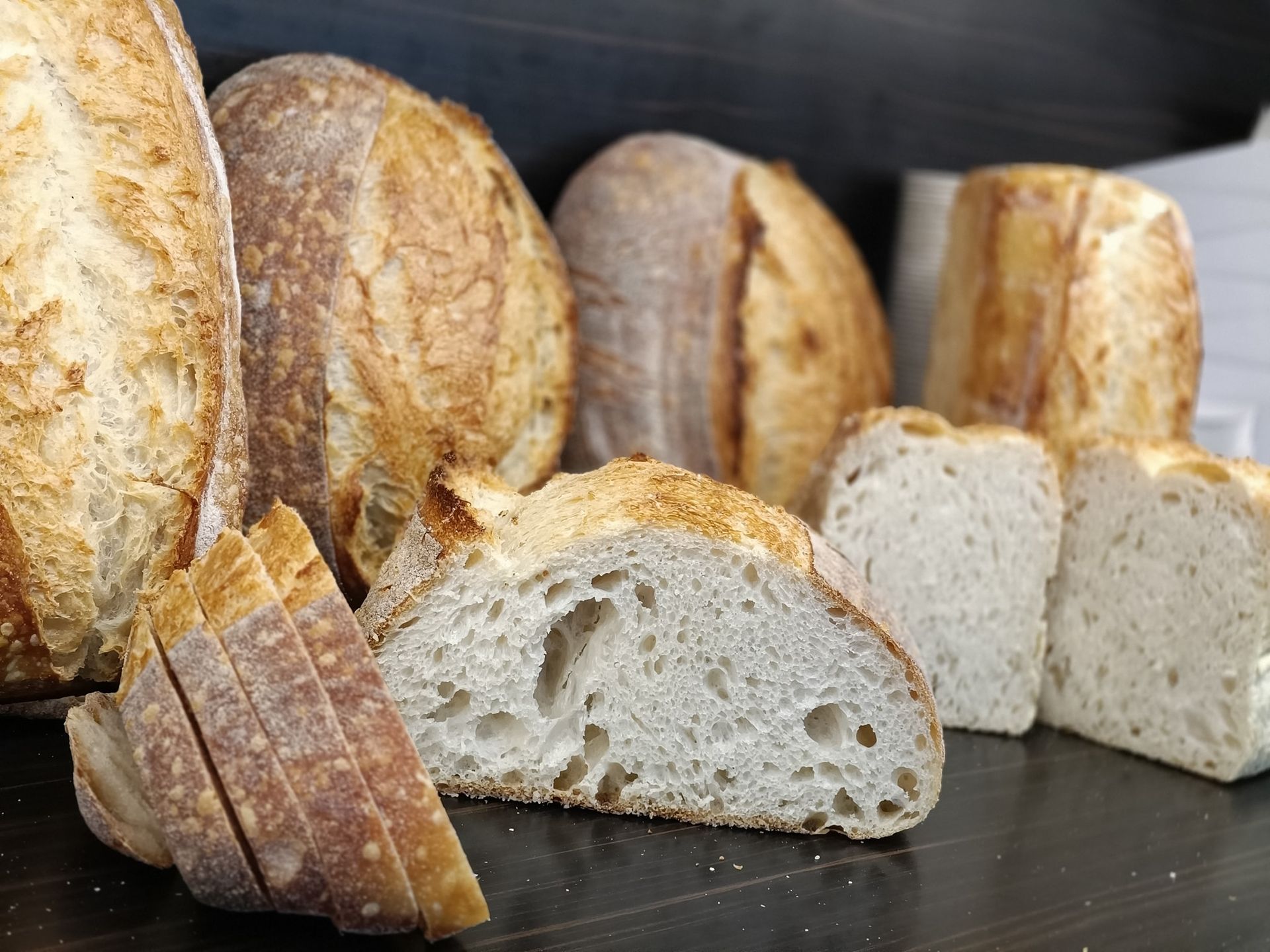 Several loaves of crusty sourdough bread, some sliced, on a dark wooden surface.— Atherton Bakehouse in Atherton, QLD