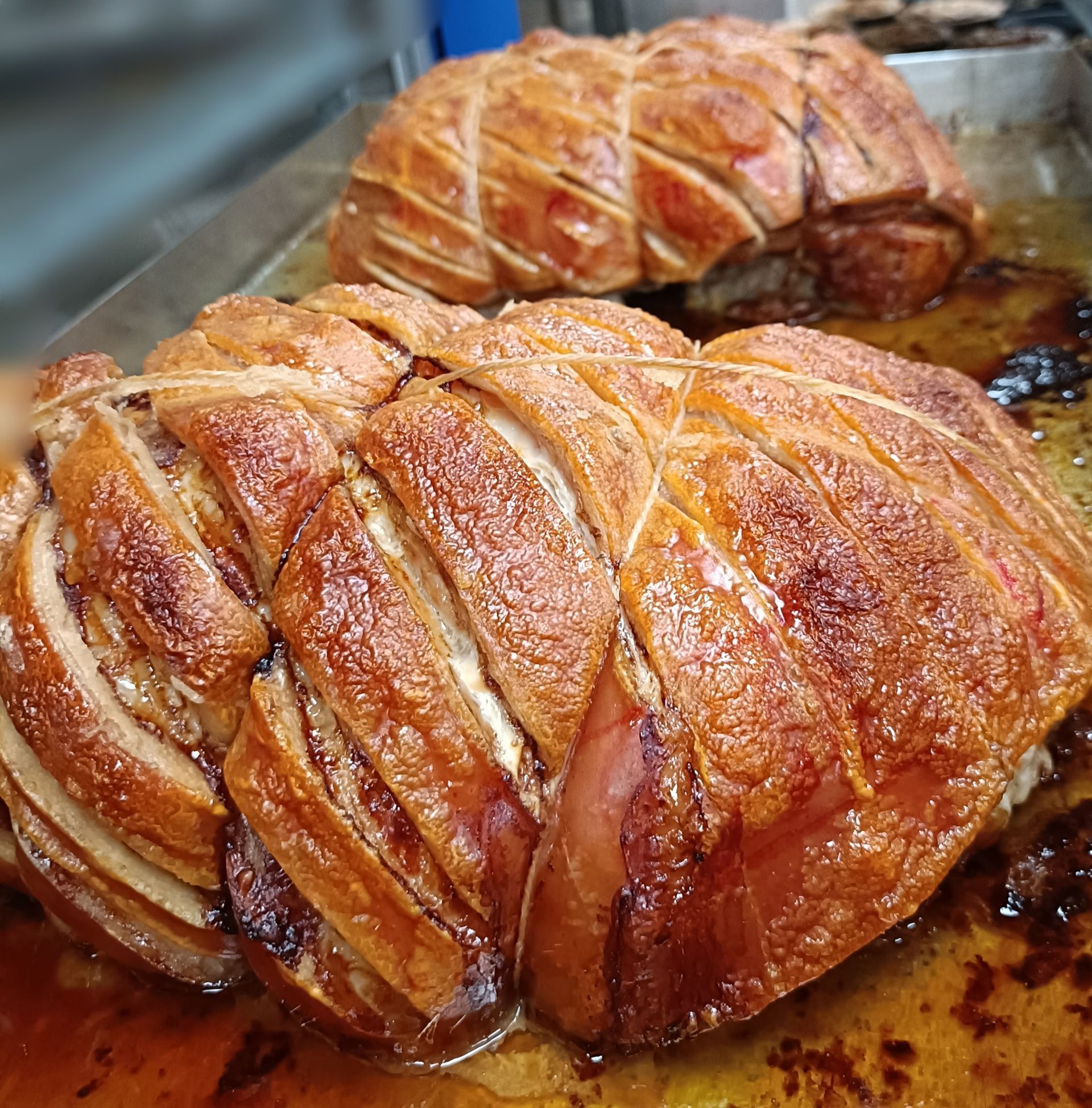 Roasted pork roast, crispy skin, tied with twine, on a metal tray.— Atherton Bakehouse in Atherton, QLD