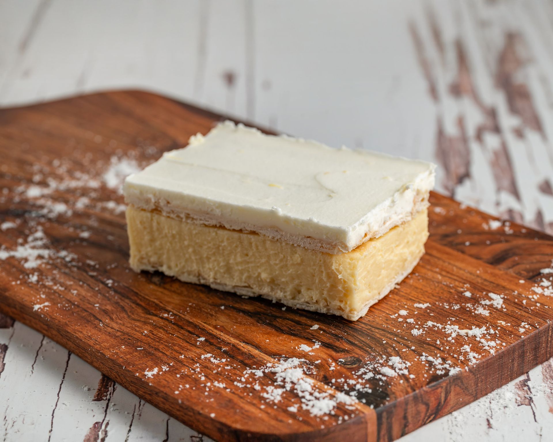 Cake slice with white frosting on a wooden board sprinkled with white powder — Atherton Bakehouse in Atherton, QLD