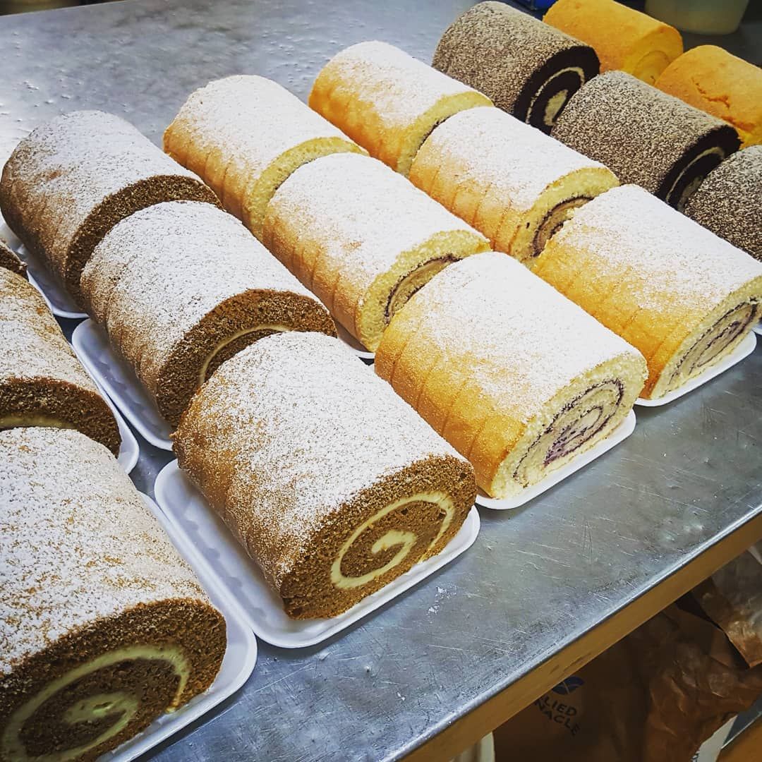 Rows of colorful swiss rolls, some dusted with powdered sugar, on a metal surface.— Atherton Bakehouse in Atherton, QLD