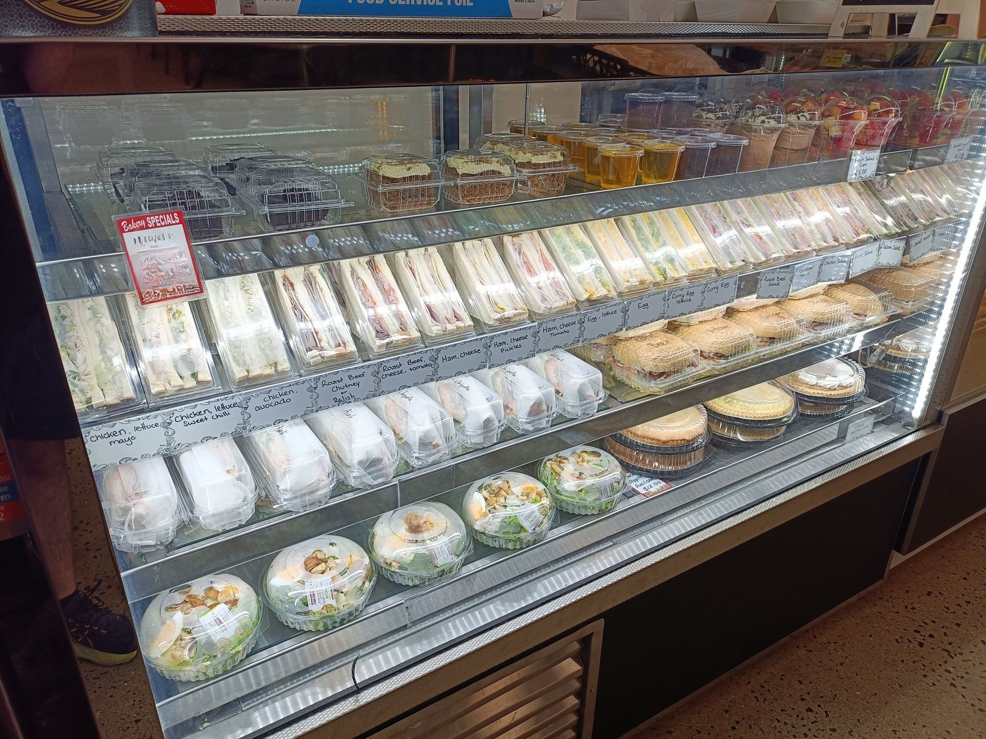 Display case filled with sandwiches, rolls, and prepared foods, illuminated from within.
