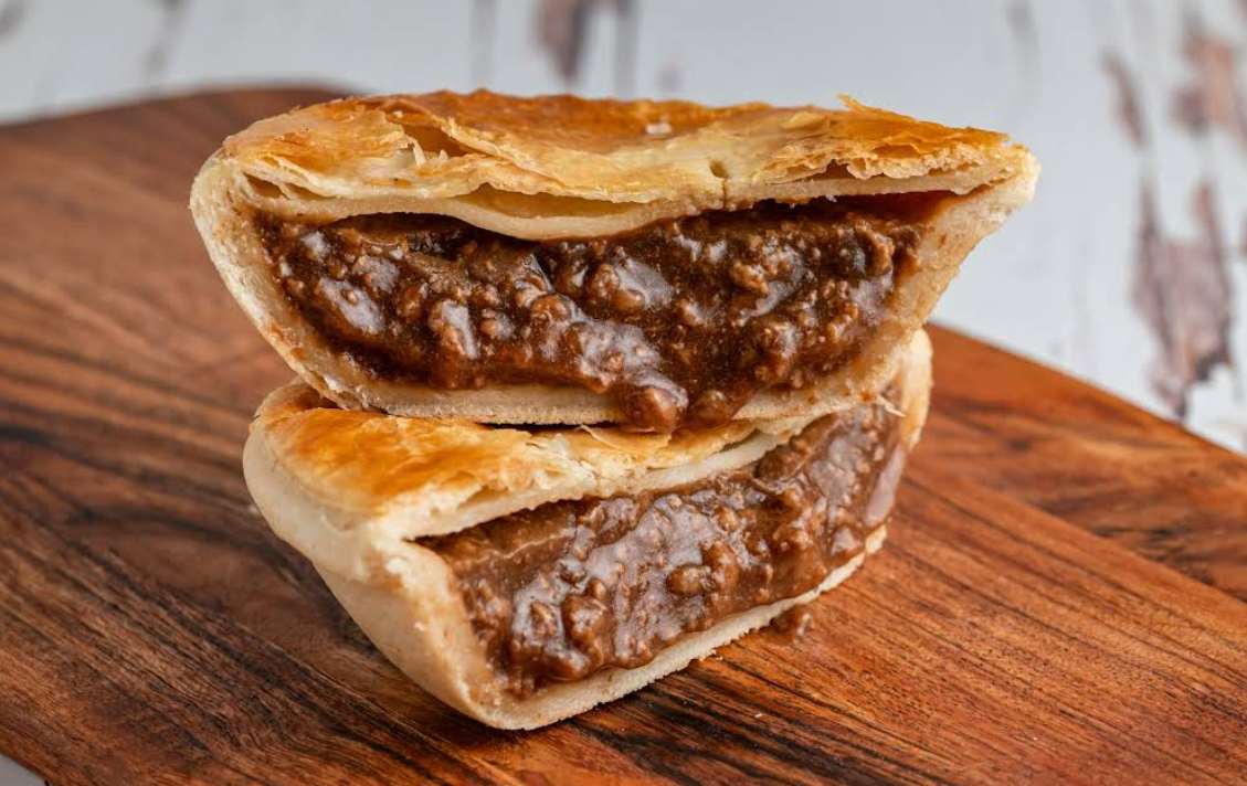 Meat pie cut in half, stacked on a wooden board; filling visible.— Atherton Bakehouse in Atherton, QLD