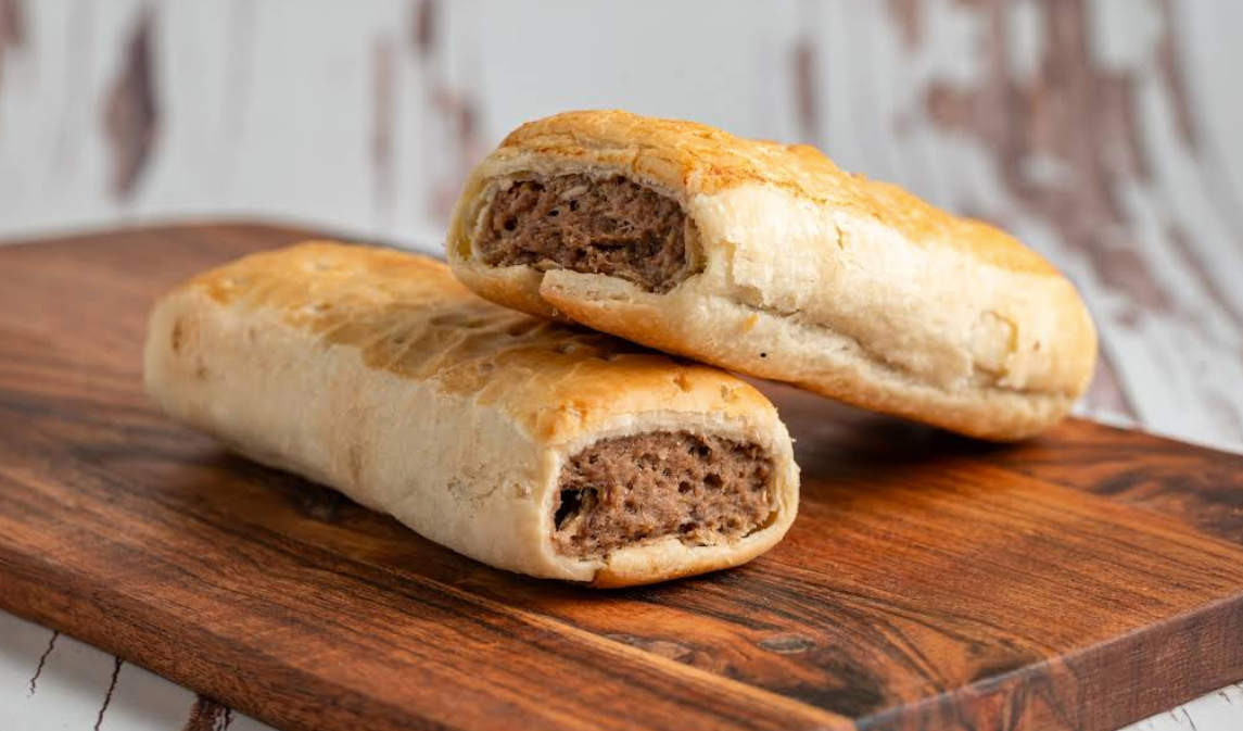 Two sausage rolls on a wooden board; baked golden pastry filled with a brown meat mixture.— Atherton Bakehouse in Atherton, QLD