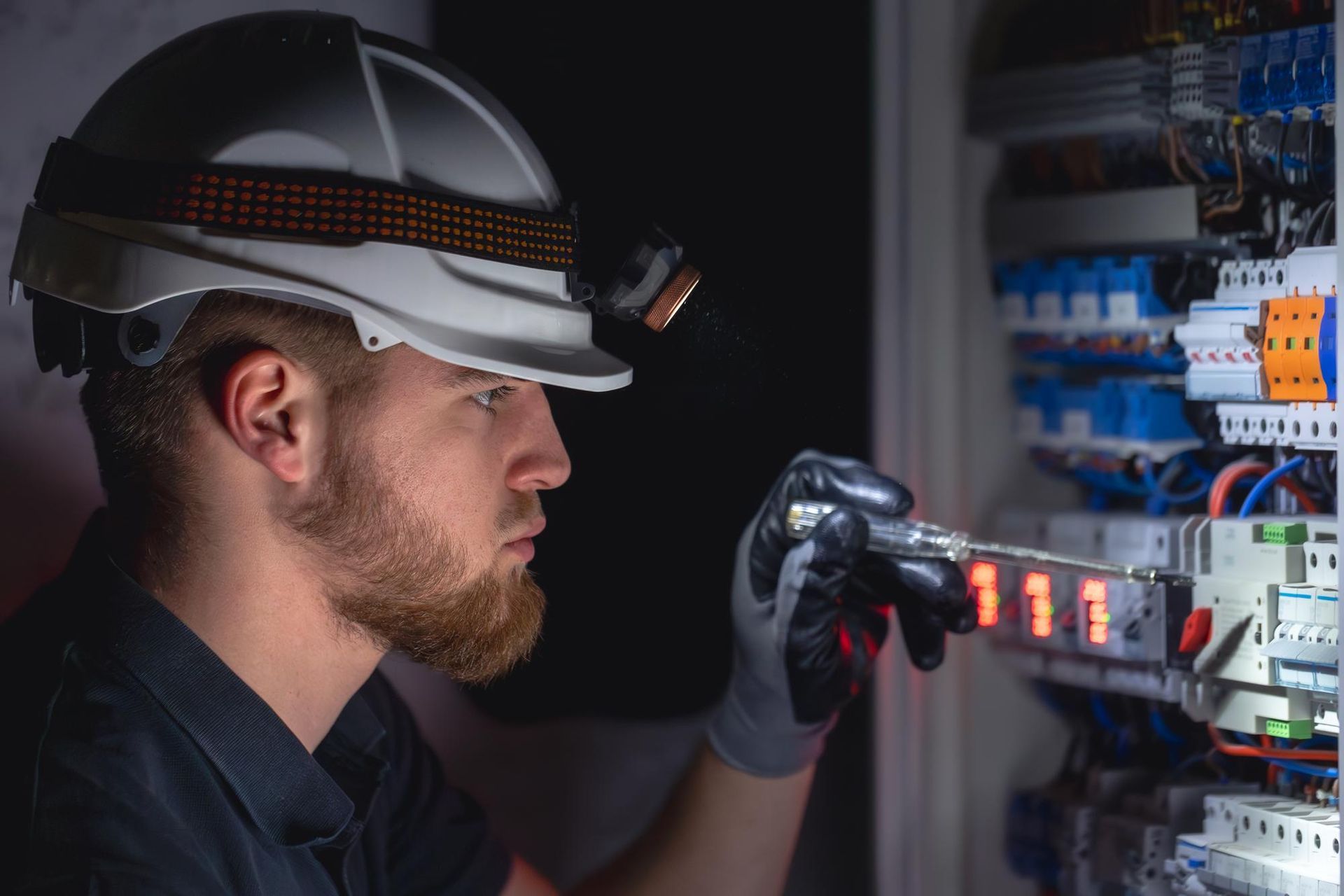Electrician with headlamp examines electrical panel.