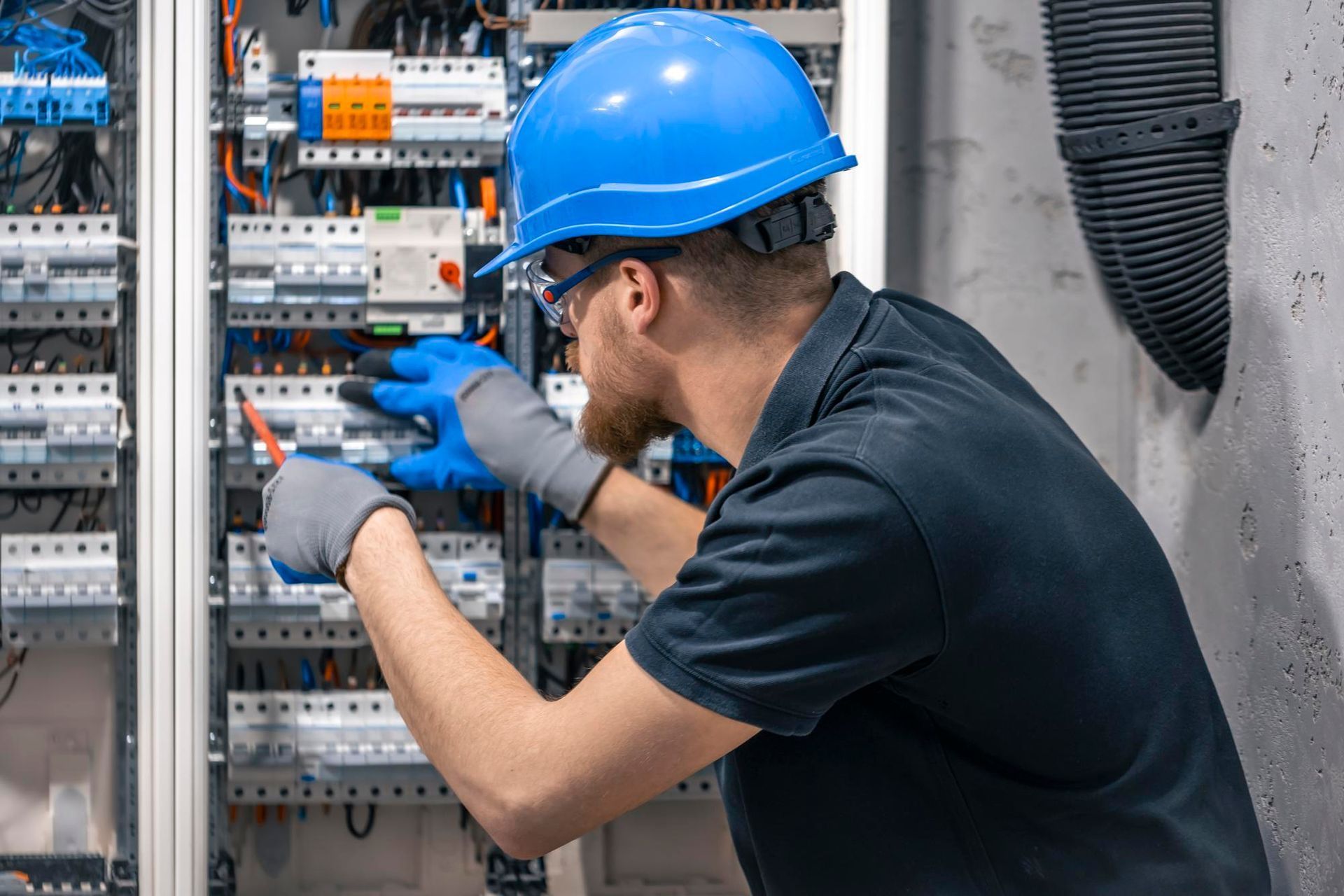 Electrician in hard hat and safety glasses working on electrical panel.