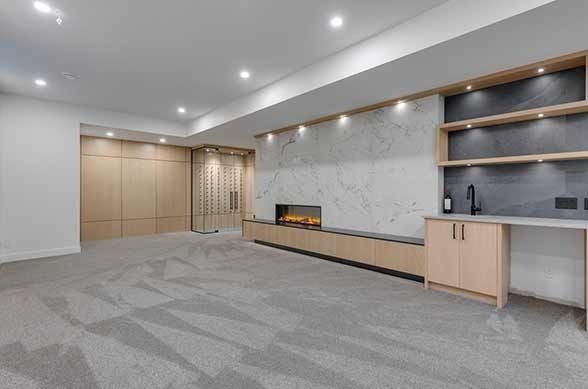 Empty modern basement with built-in cabinetry, fireplace, and bar area. Light wood and gray accents.