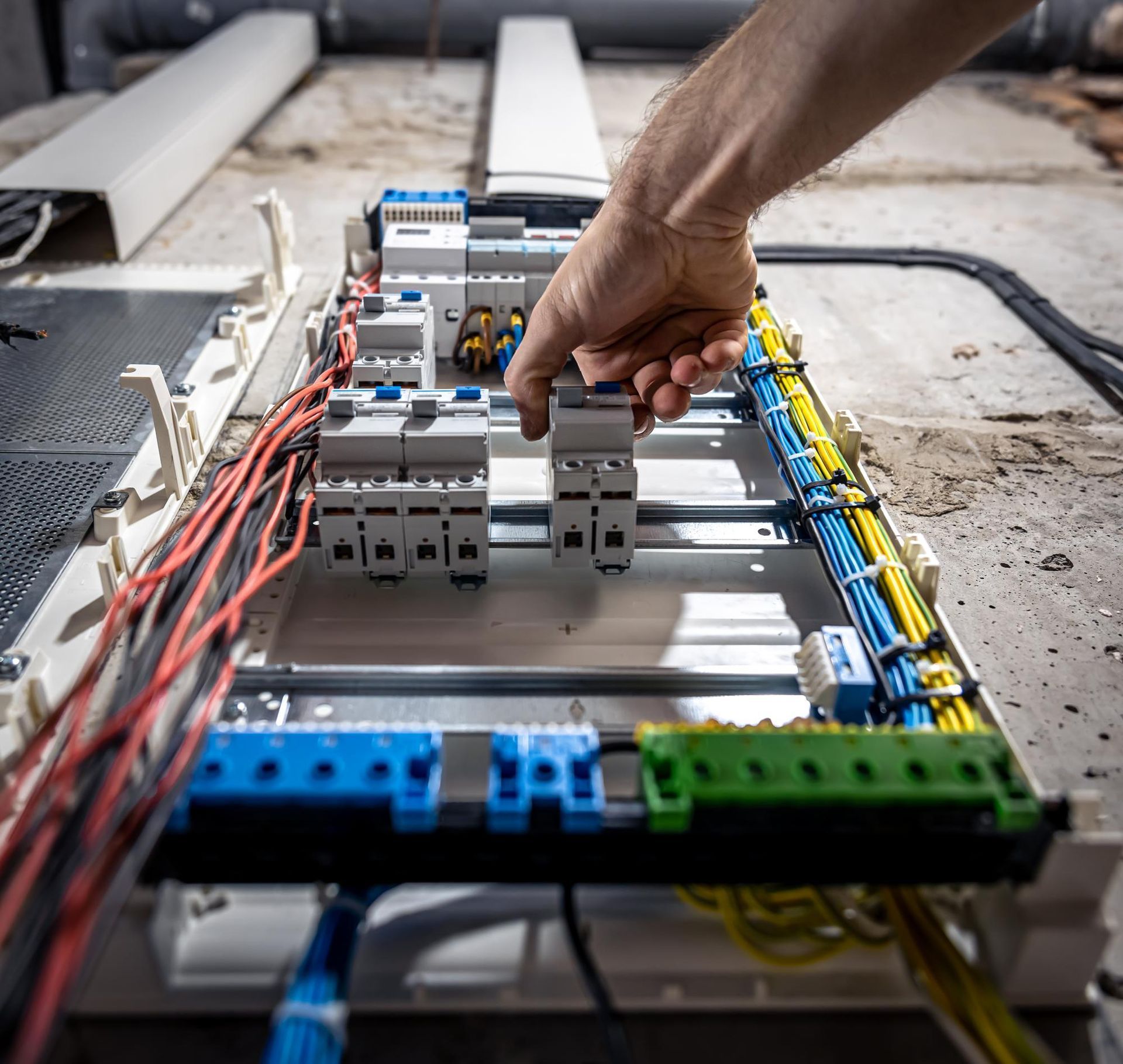 A hand adjusting a circuit breaker in an electrical box, wires are visible.