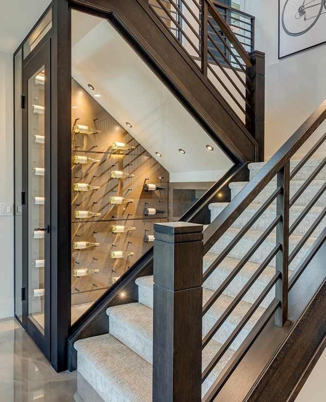 Wine storage built into the stairwell, dark wood frame, angled storage, glass door, warm lighting, contemporary design.