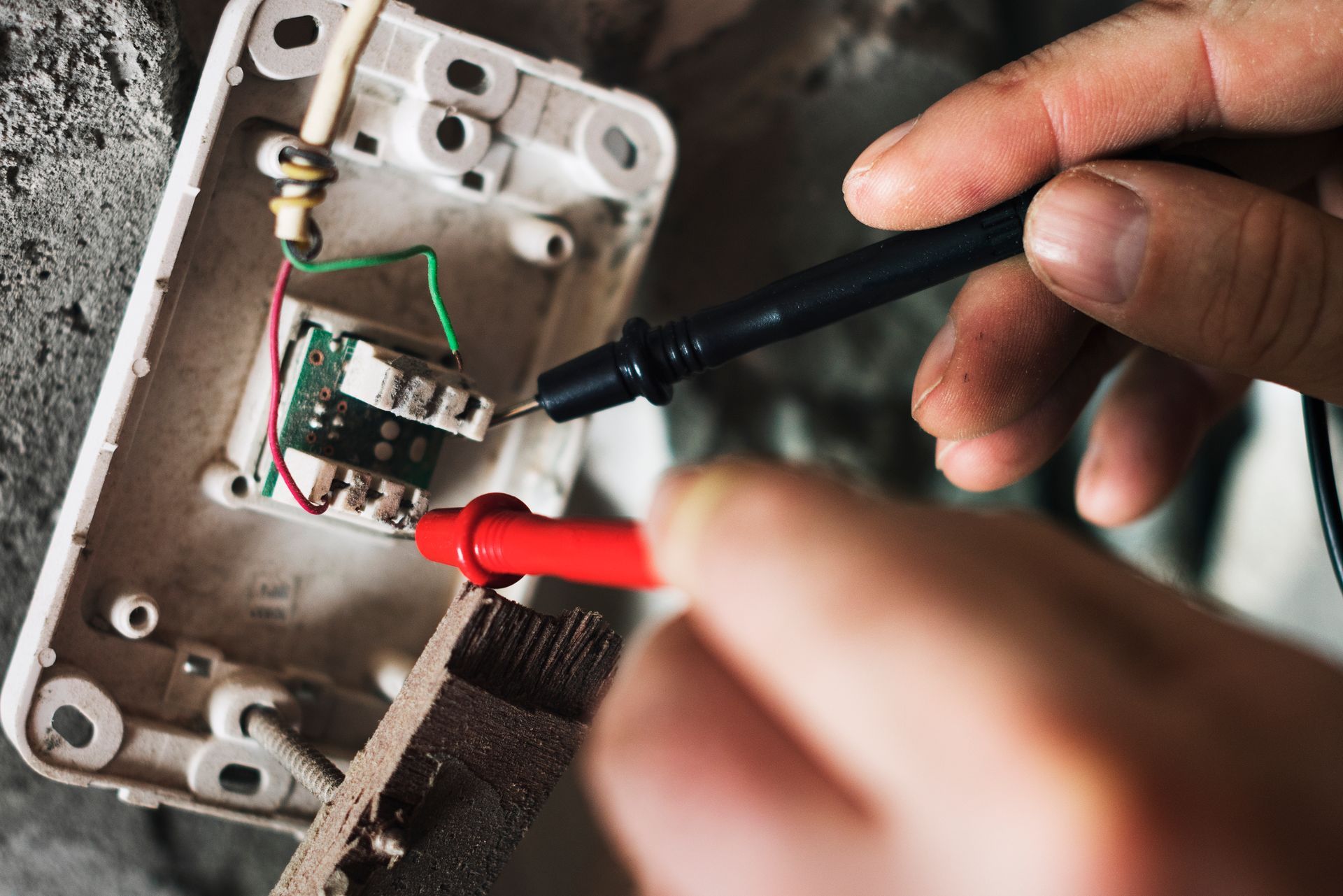 Hands testing wires of an open electrical component with red and black probes.
