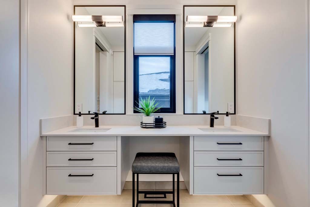 Modern bathroom with two mirrors, vanities, black accents, and a stool.