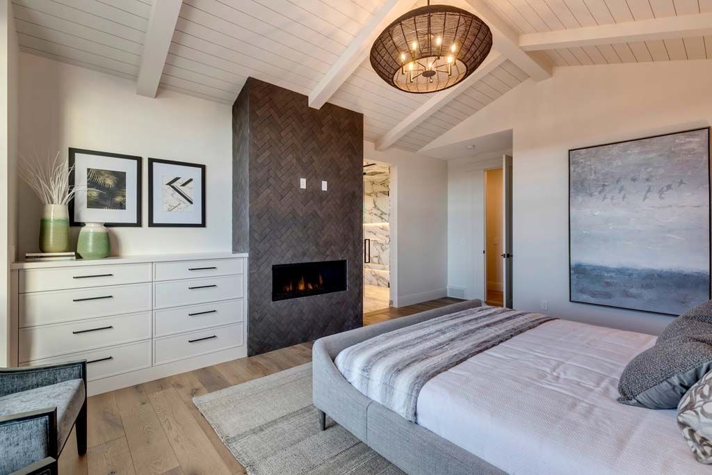 Modern bedroom with fireplace, light wood floor, white ceiling beams, and artwork.