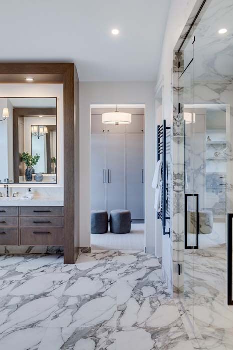 Luxurious bathroom with marble floors, walk-in shower, vanity, and walk-in closet in the background.