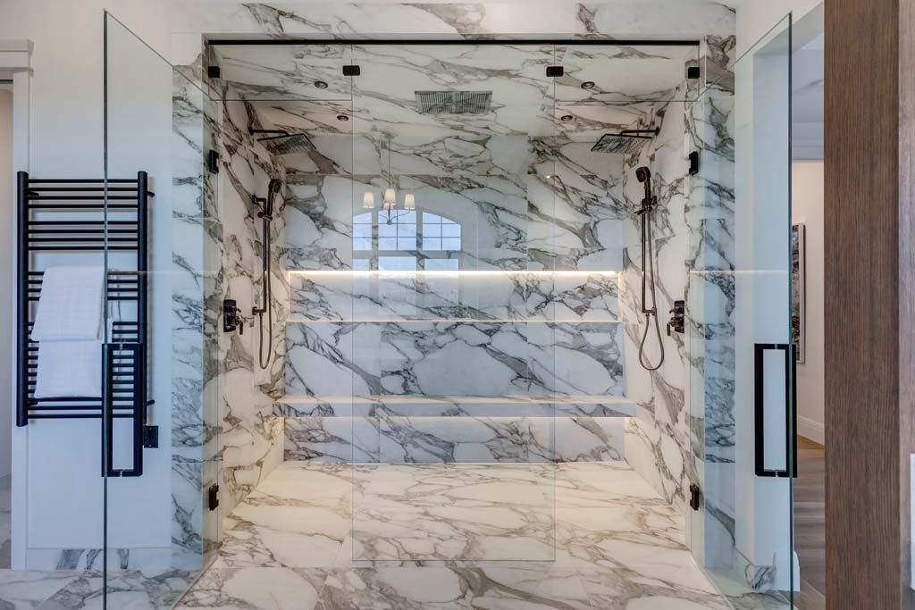 Spacious, marble-tiled shower with glass doors and black fixtures; heated towel rack on left.