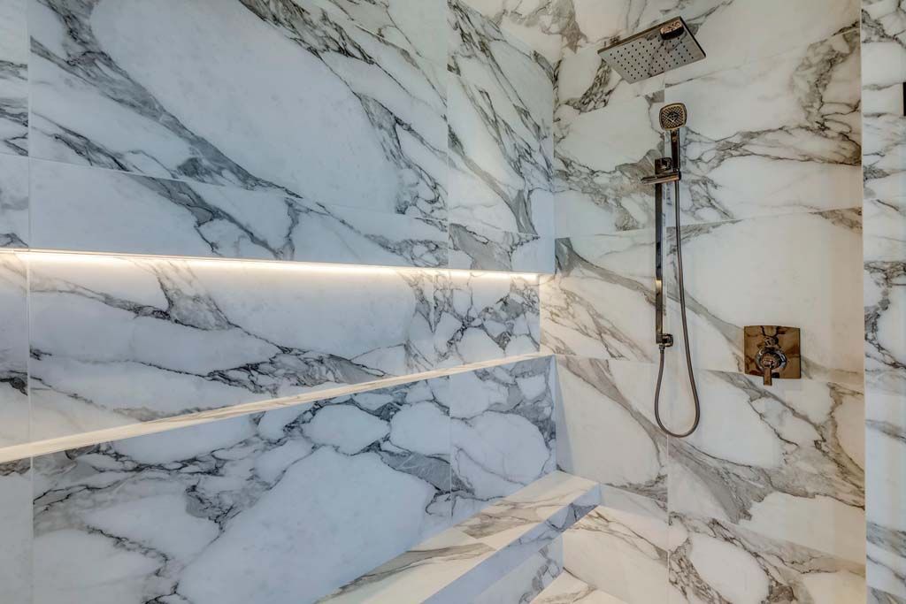 Luxurious marble shower with recessed shelf and showerhead.