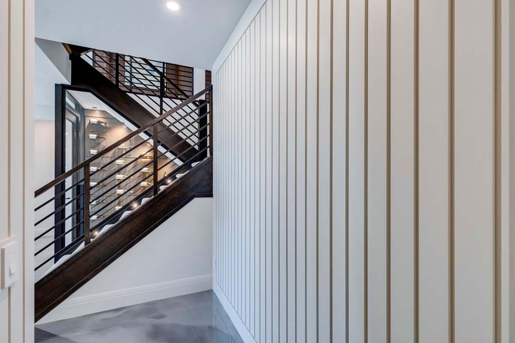 Hallway with white vertical paneling, dark wood staircase with metal railing, and concrete floor.