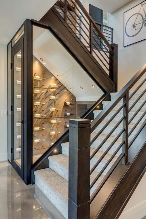 Staircase with built-in wine cellar; dark wood, metal railing, neutral carpeted stairs, bottles illuminated inside the cellar.