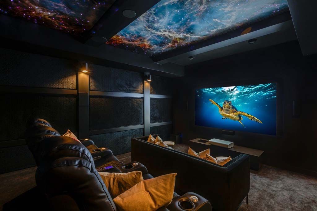 Home theater with a starry ceiling, large screen showing a sea turtle, and black leather seating.